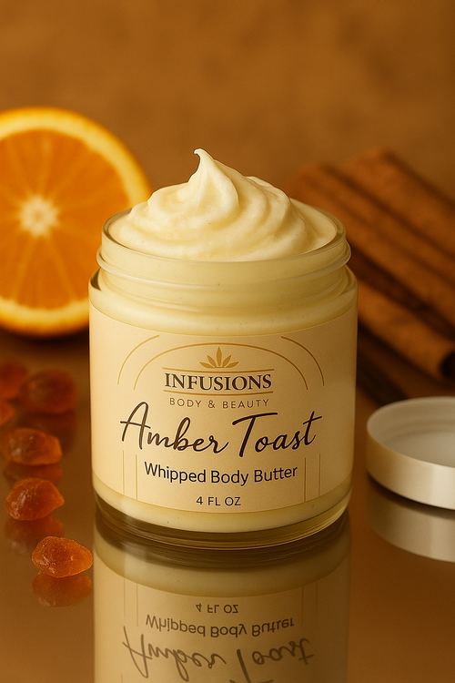 Jar of Infusions Amber Toast Whipped Body Butter with an orange, cinnamon stick, and amber gummy bears on a reflective surface.